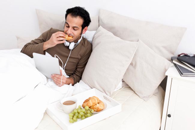 Man with tablet computer eating in bed